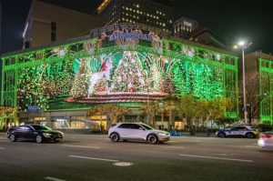 Jung-gu, Seoul, South Korea - November 19, 2023: Night view of cars on the road against christmas trees and green LED light of media façade on the wall of Shinsegae Department Store